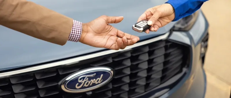 Ford vehicle key fob being handed over in front of a Ford grille — fleet delivery at Envision Motors Fleet