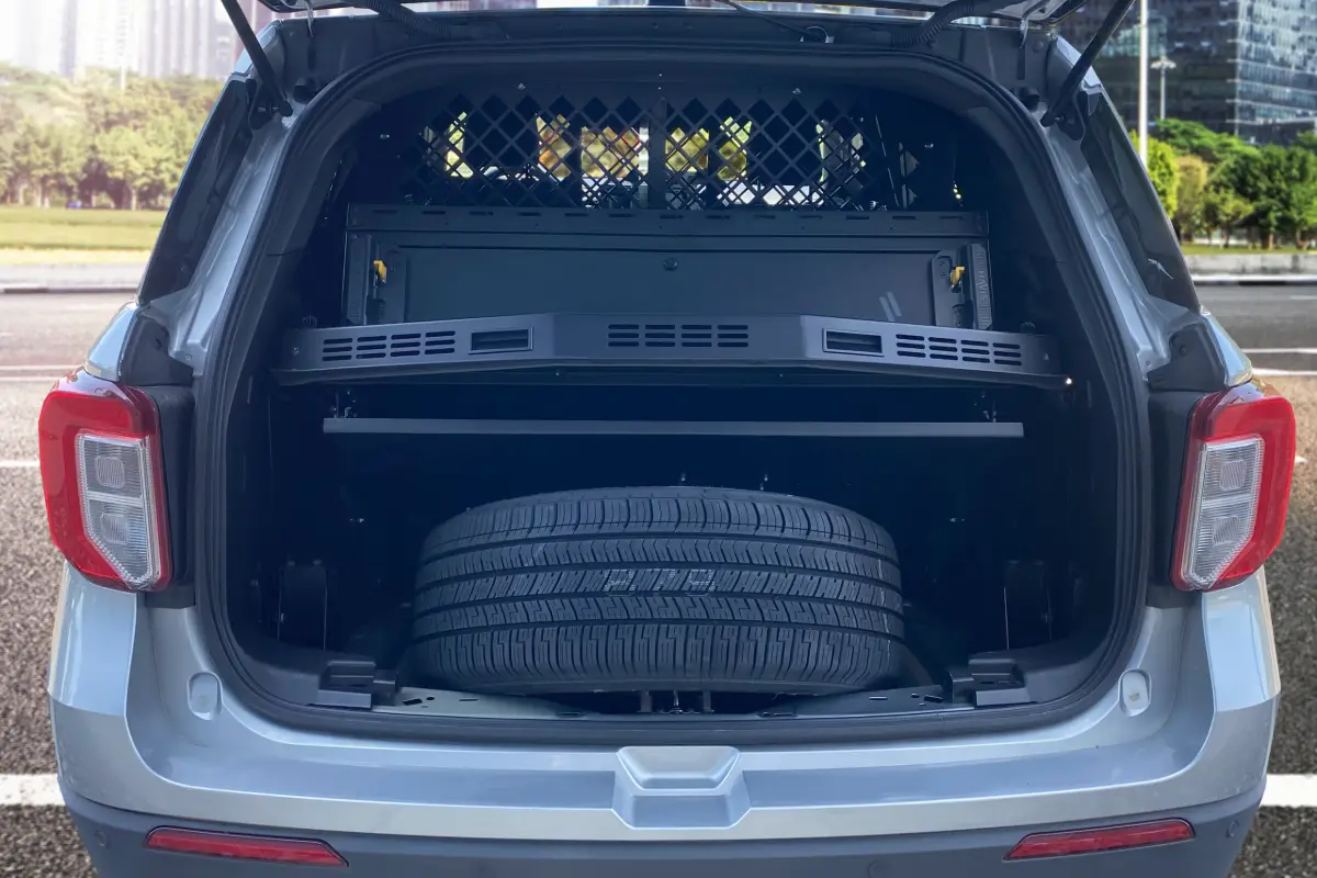 Rear cargo area of a Ford Police Interceptor Utility fitted with a cargo barrier and an equipment shelf above the spare wheel